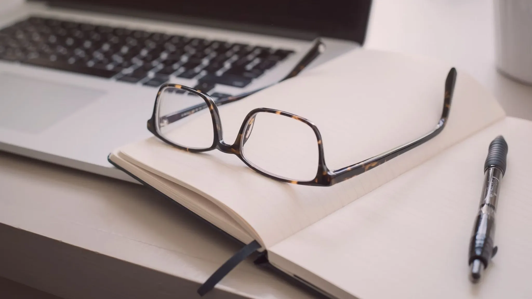 Glasses, blank notebook, and laptop on a desk,
